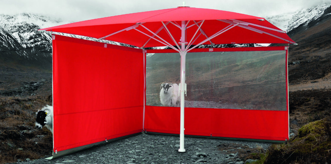Bahama Sonnenschirm mit Seitenwänden steht in Berglandschaft mit Schafen.