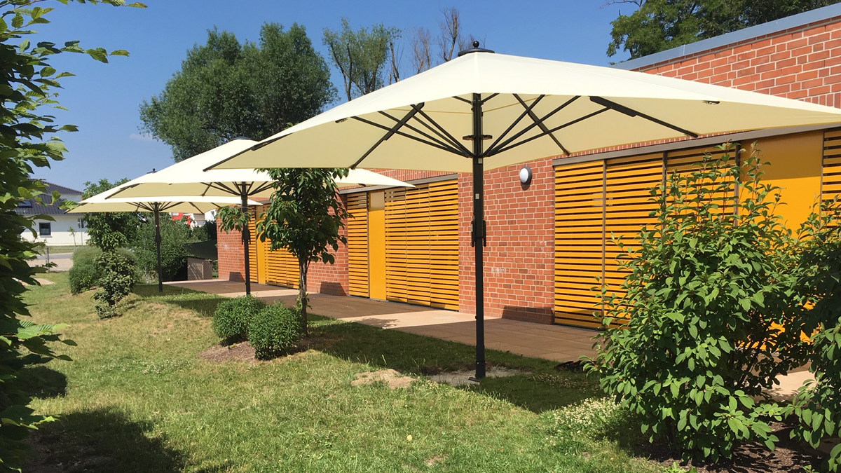 3 Bahama Jumbrella Sonnenschirme auf einer Wiese vor einem Haus.